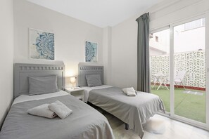 Une chambre d’hôtel avec deux lits, une table de chevet avec une lampe et une porte-fenêtre coulissante donnant sur un espace extérieur.