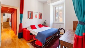 Une chambre moderne avec un lit, des rideaux rouges et bleus, une table en bois et une fenêtre.