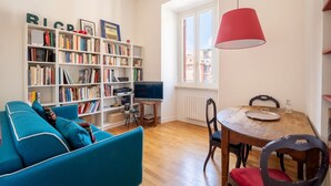 Un salon comprenant une bibliothèque, un canapé bleu, une table à manger en bois avec des chaises et un luminaire suspendu rouge.