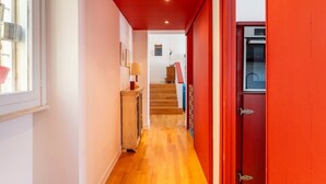 Un couloir avec un plancher en bois, une porte rouge et un escalier menant à une autre pièce.