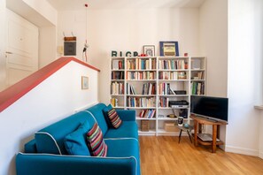 Un salon avec un canapé bleu, une bibliothèque, un téléviseur et un plancher en bois.