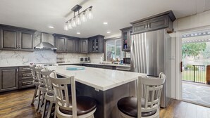 A modern kitchen with a large island, dark cabinets, stainless steel appliances, and a view to the outdoors. - House right on the lake w/ hot tub, kayak, SUP & games - great location (Shelton)