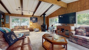 A cozy living room with a fireplace, leather sofas, a coffee table, and a large TV. - House right on the lake w/ hot tub, kayak, SUP & games - great location (Shelton)
