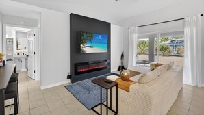 Una sala de estar moderna con televisor de pantalla plana, chimenea, ventilador de techo y vistas al exterior.