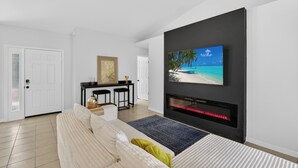 Una sala moderna con una televisión de pantalla plana montada en la pared, una chimenea, un sofá y un comedor con una mesa y sillas.
