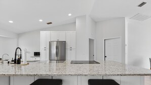 Una cocina moderna con armarios blancos, un refrigerador de acero inoxidable y una encimera de granito.