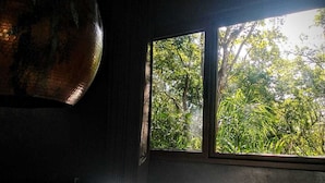 Une chambre avec un grand lit, une fenêtre donnant sur un paysage verdoyant et un ventilateur de plafond.