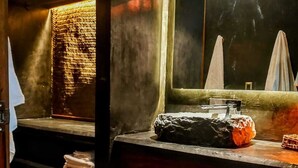 Une salle de bain avec un comptoir en bois, un lavabo et un miroir. On y trouve un porte-serviettes avec des serviettes pliées et un tapis à motifs sur le sol.