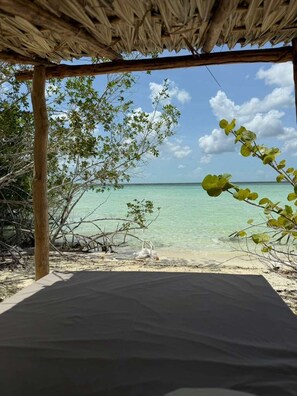 A beach view with a thatched roof structure, clear turquoise water, and lush greenery. - Casa Vive Bacalar (Bacalar)
