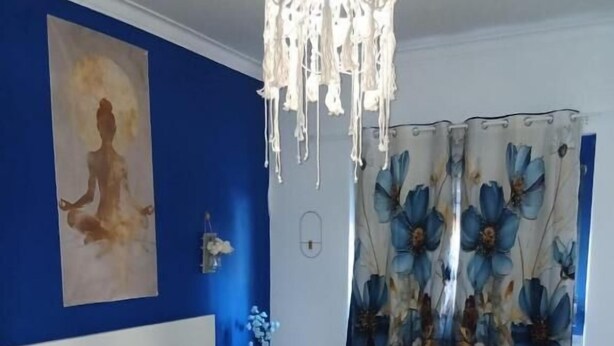 A bedroom with a bed, a hanging light fixture, a wall painting, and a floral curtain. - Macarena AL (Almada)