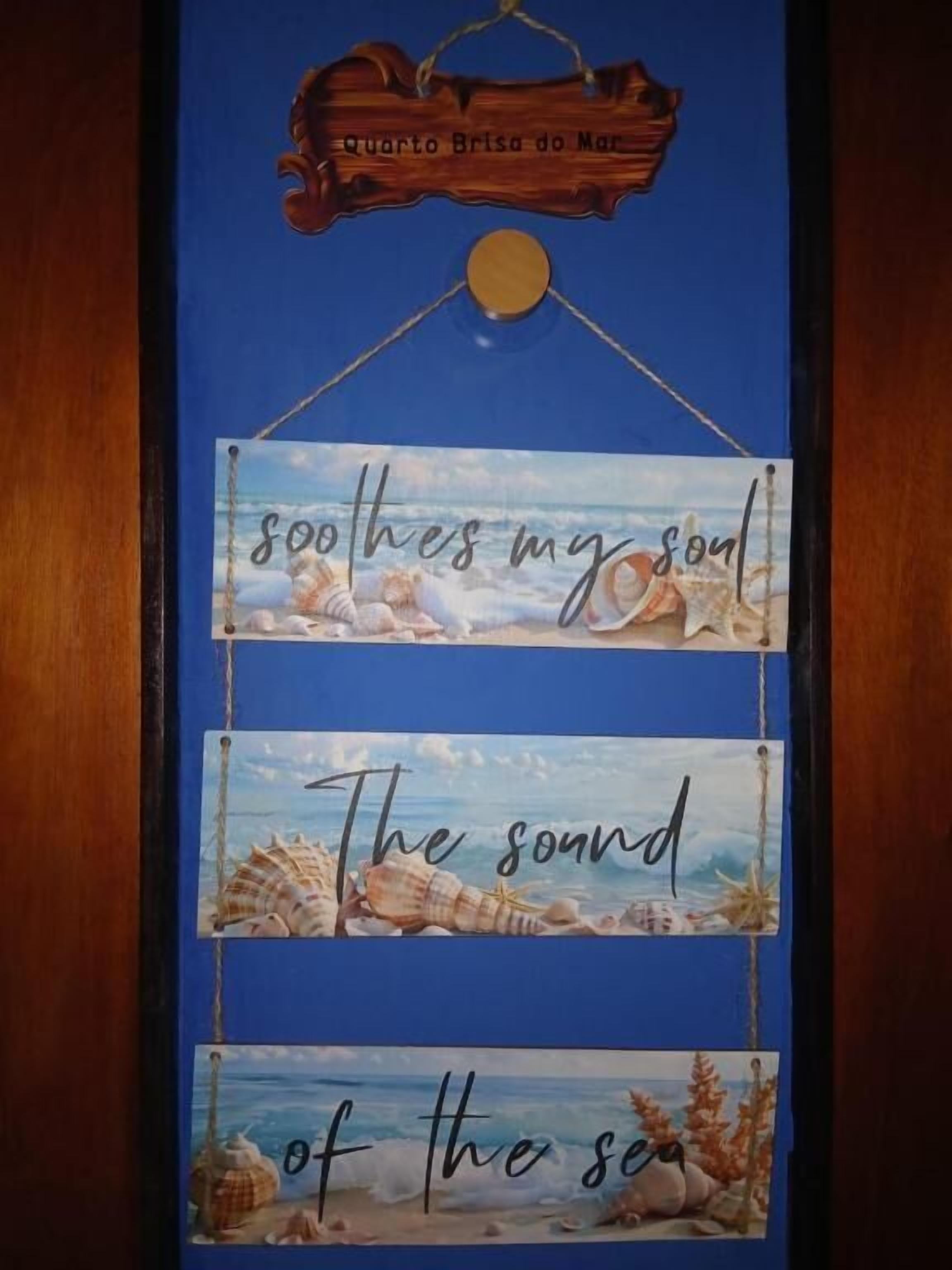 A wooden sign with the text "Quarto Brisa do Mar" and a hanging decoration with the phrase "soothes my soul" and "The sound of the sea".