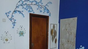 A room with a wooden door, a blue accent wall, and decorative wall art including a white flower arrangement and a textured panel. - Macarena AL (Almada)