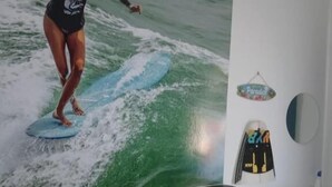 A room with a large mural of a surfer on a wave, a wooden cabinet with drawers, a white cabinet, and a small round mirror on the wall. - Macarena AL (Almada)