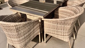 Un patio al aire libre con una mesa de vidrio rodeada de sillas de mimbre.