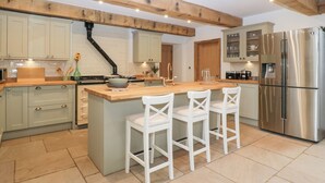 Une cuisine moderne dotée d’un îlot central, de tabourets de bar blancs, d’appareils électroménagers en acier inoxydable et de poutres en bois apparentes.