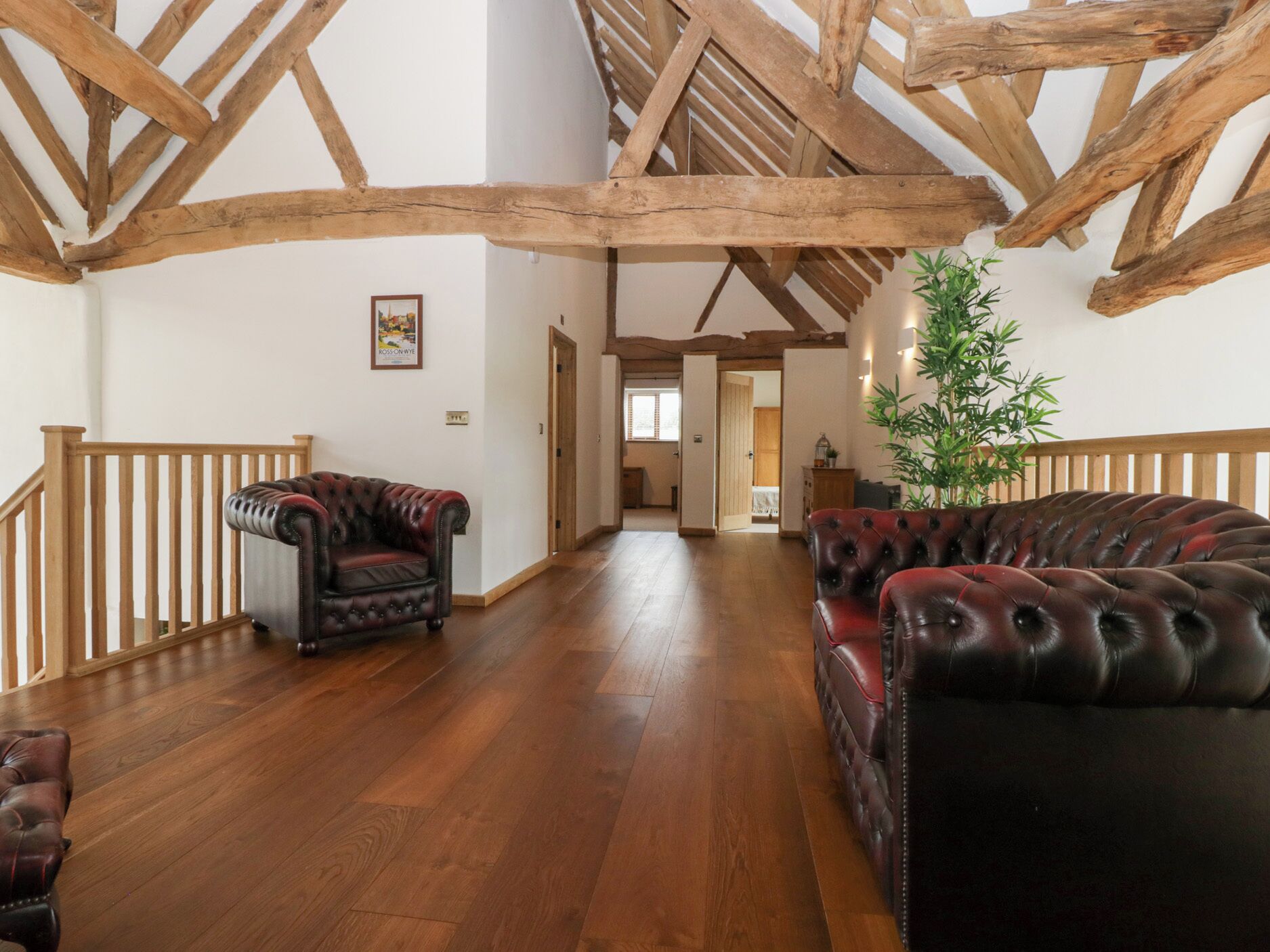 A spacious room with wooden beams, a leather sofa, a chair, and a potted plant.