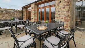 Une terrasse extérieure avec un mur en pierre, une porte vitrée et une table avec des chaises.