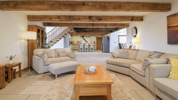 Un vaste espace de vie comprenant deux canapés, une table basse en bois et un escalier menant à un niveau supérieur.