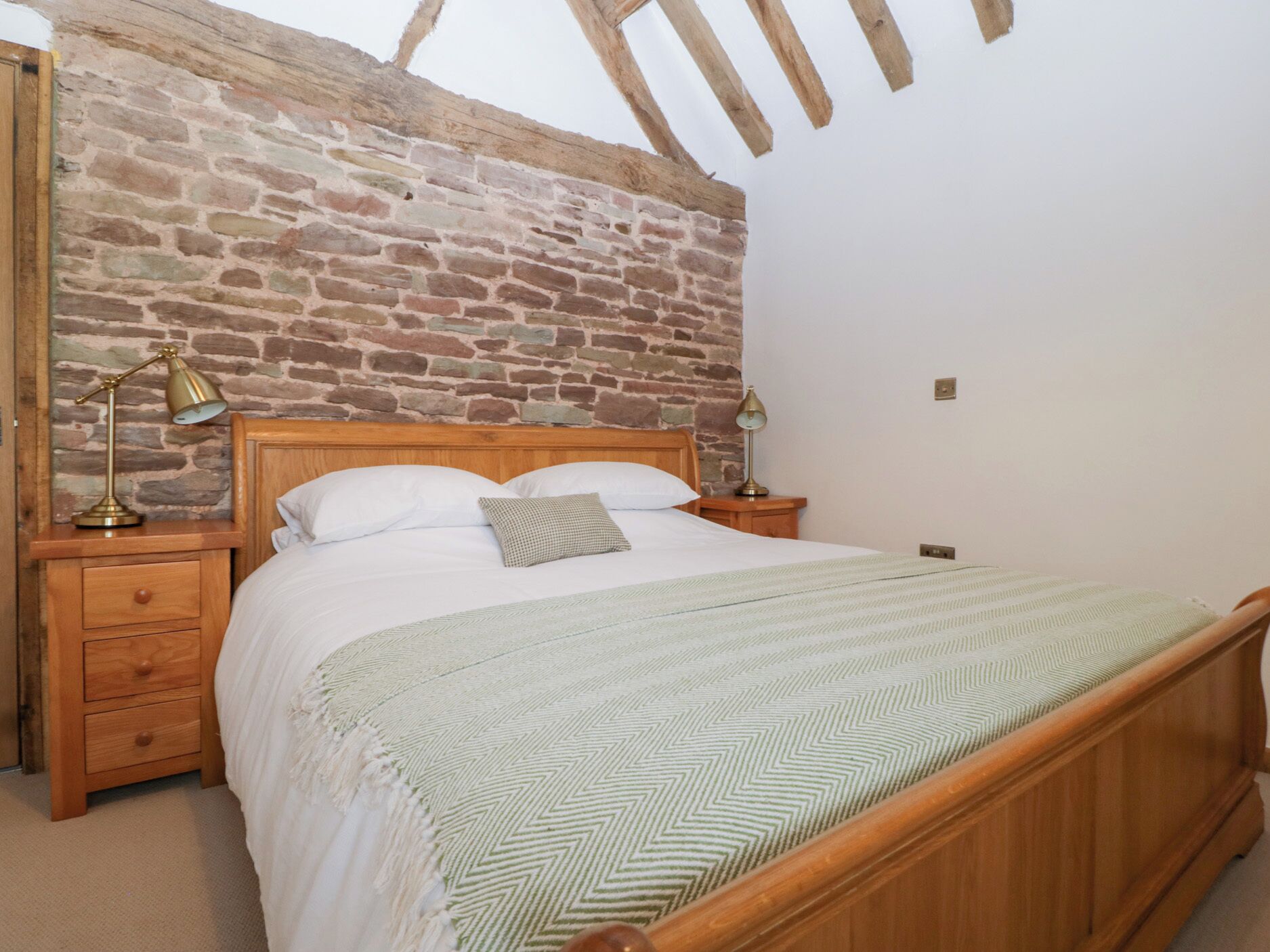 A bedroom with a wooden bed, a brick wall, and a sloped ceiling.