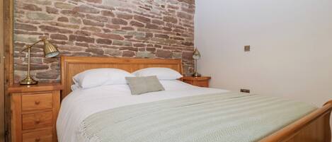 A bedroom with a wooden bed, a brick wall, and a sloped ceiling.