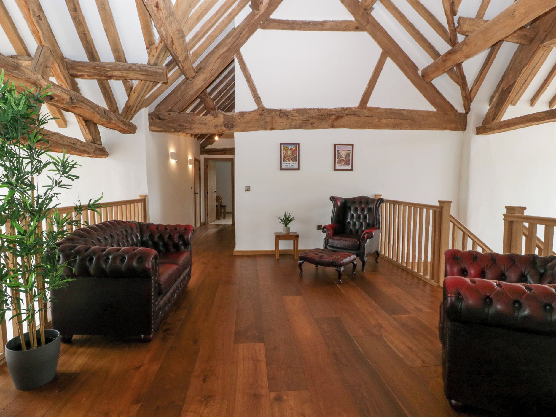 A spacious room with wooden beams, a leather sofa, a chair, and a potted plant.