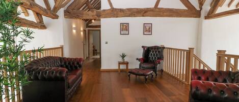 A spacious room with wooden beams, a leather sofa, a chair, and a potted plant.