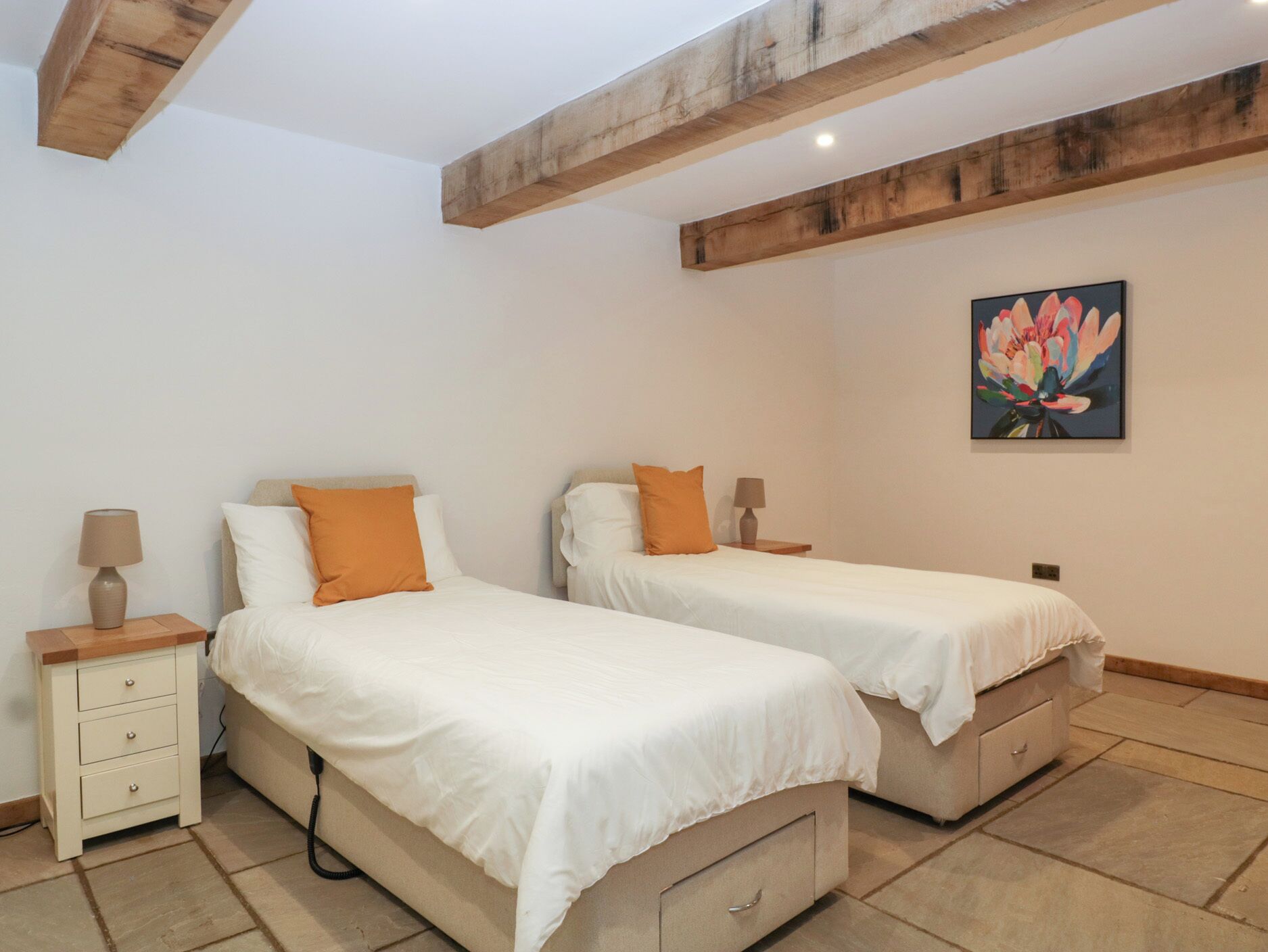 Une chambre avec deux lits, des poutres en bois au plafond, une table de chevet avec une lampe et un tableau au mur.