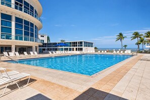 A swimming pool with lounge chairs and a building with large windows in the background.