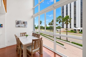 A dining area with a table and chairs, large windows with a view of palm trees and a building.