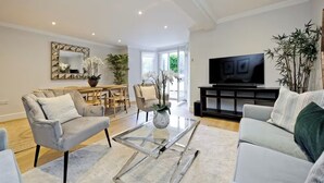 A modern living room with a sofa, armchairs, a coffee table, and a TV. - Stunning garden apartment in heart of Kensington (London)