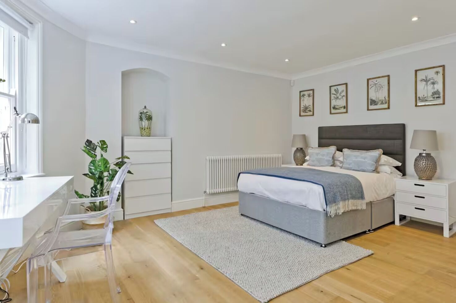 A bedroom with a bed, bedside tables, a desk, a chair, and a radiator.