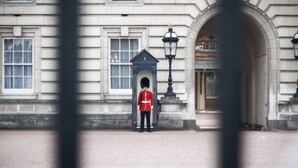 A uniformed guard standing in front of a building with a large archway and a lamp post. - Stunning garden apartment in heart of Kensington (London)