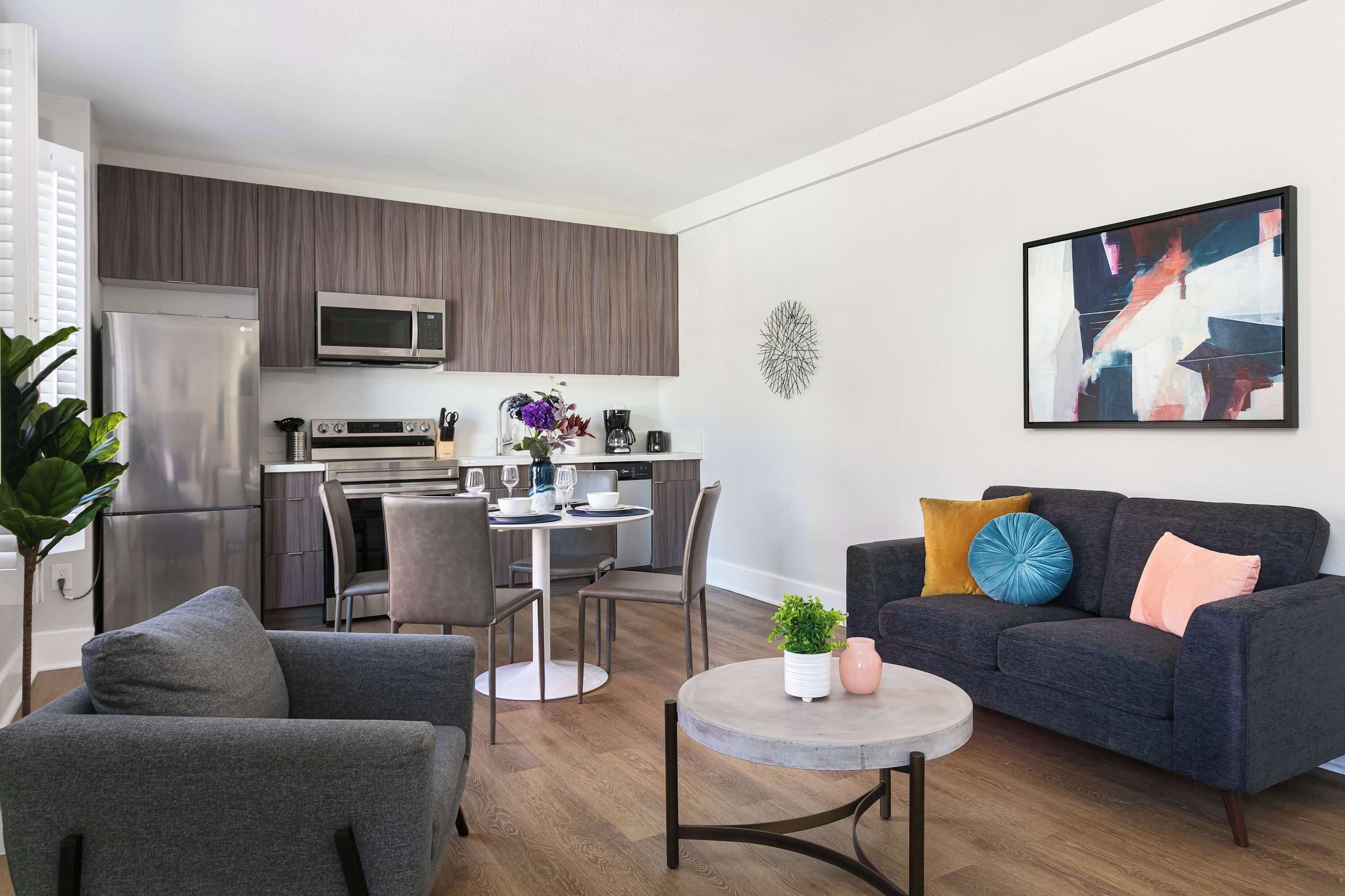 A modern living room with a grey sofa, a round coffee table, and a dining area with a white table and chairs.