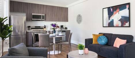 A modern living room with a grey sofa, a round coffee table, and a dining area with a white table and chairs.