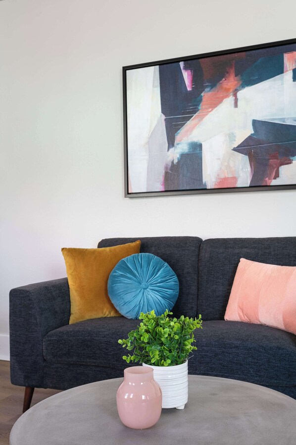 A modern living room with a grey sofa, a round coffee table, and a framed abstract painting on the wall. - The Penn Hotel - Central 2BR Hotel Suite Stay in Historic Gaslamp (San Diego)