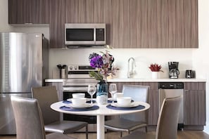 A modern kitchen with a dining area, stainless steel appliances, and a vase with flowers. - The Penn Hotel - Central 2BR Hotel Suite Stay in Historic Gaslamp (San Diego)