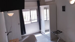 Ein Zimmer mit Bett, Schreibtisch, Stuhl, Fernseher, einem Fenster mit Vorhängen und einer Klimaanlage.