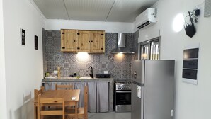 Eine kleine Küche mit Holzausstattung, einem Edelstahlkühlschrank, einem Gaskochfeld und einem Essbereich mit einem Holztisch und Stühlen.