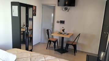 Hotellihuone, jossa on sänky, seinälle asennettu televisio, pieni pöytä tuoleineen ja kahvinkeitin.
