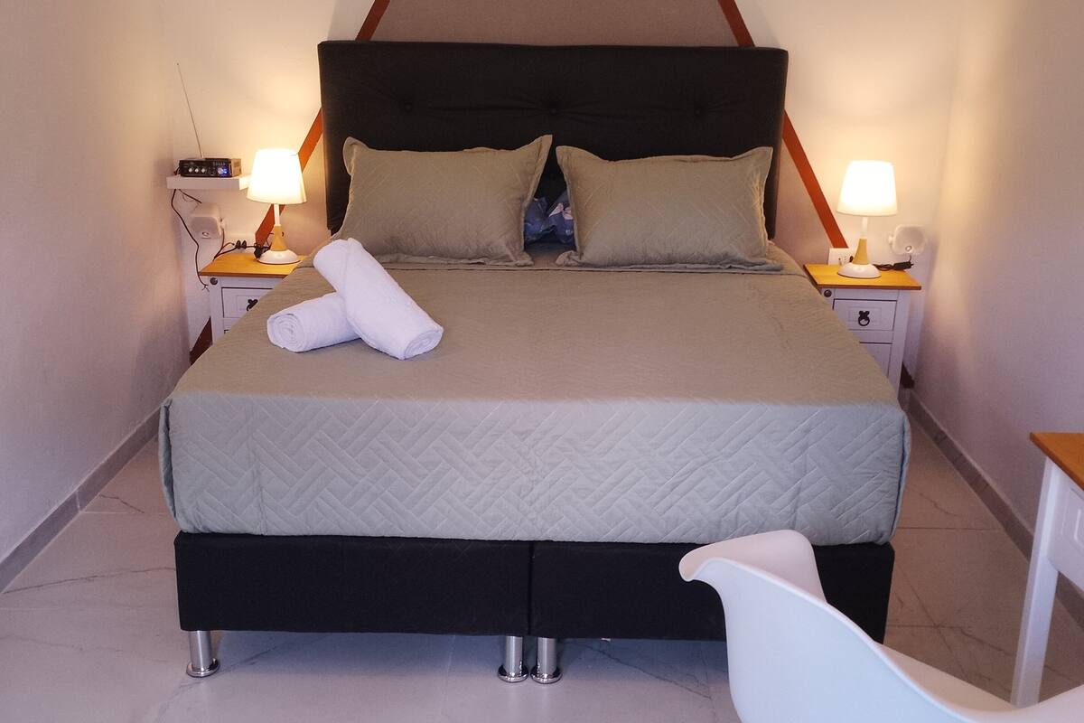 A neatly made bed with a quilted headboard, two bedside lamps, a white chair, and a small table.