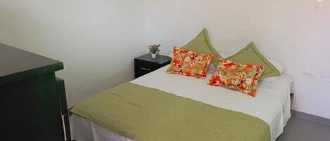 Un dormitorio con una cama, almohadas verdes, una mesita de noche con una planta y un escritorio verde.