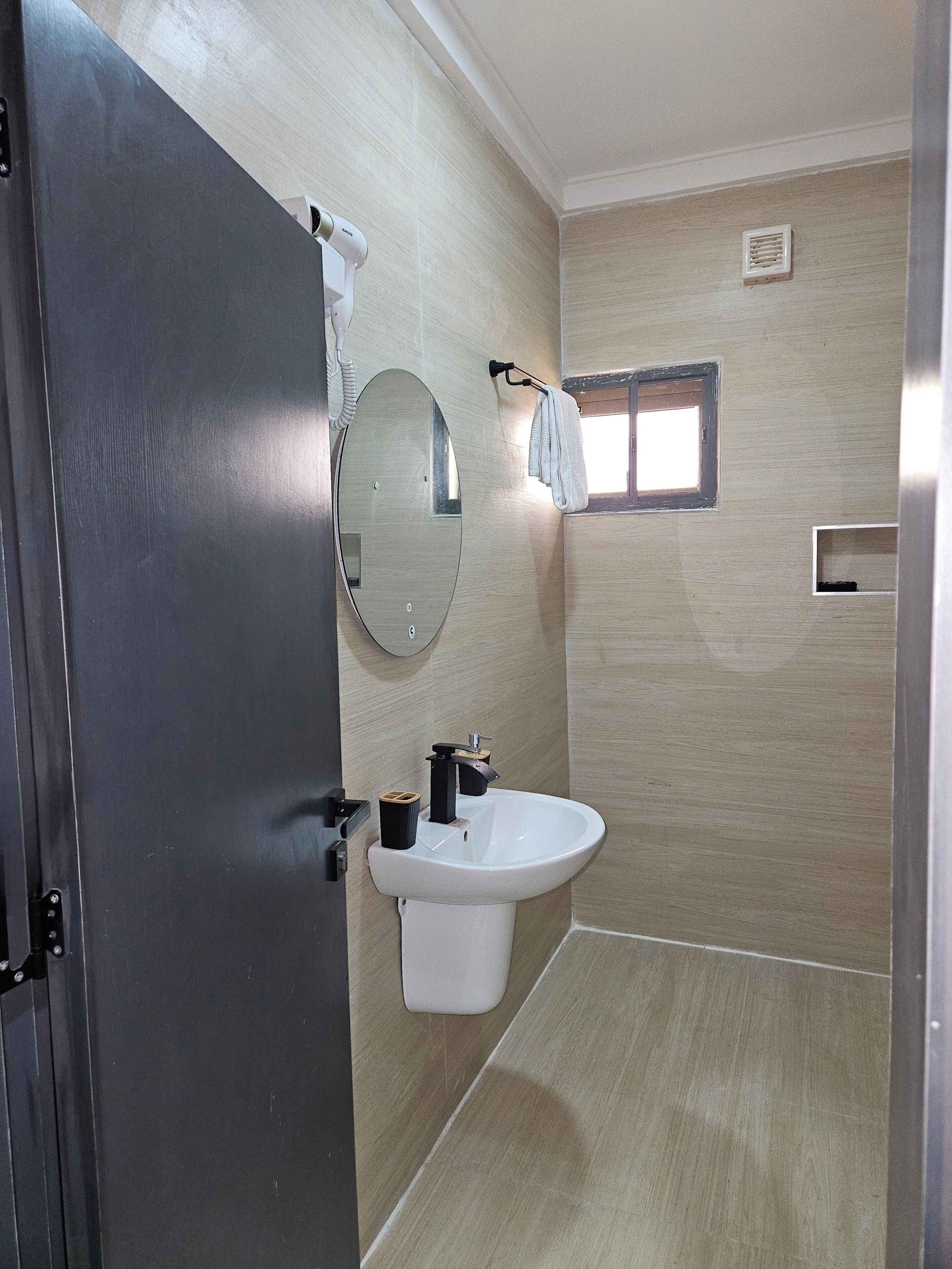 Un baño con lavamanos, espejo, toallero y un ventanal pequeño.