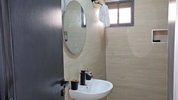 Un baño con lavamanos, espejo, toallero y un ventanal pequeño.