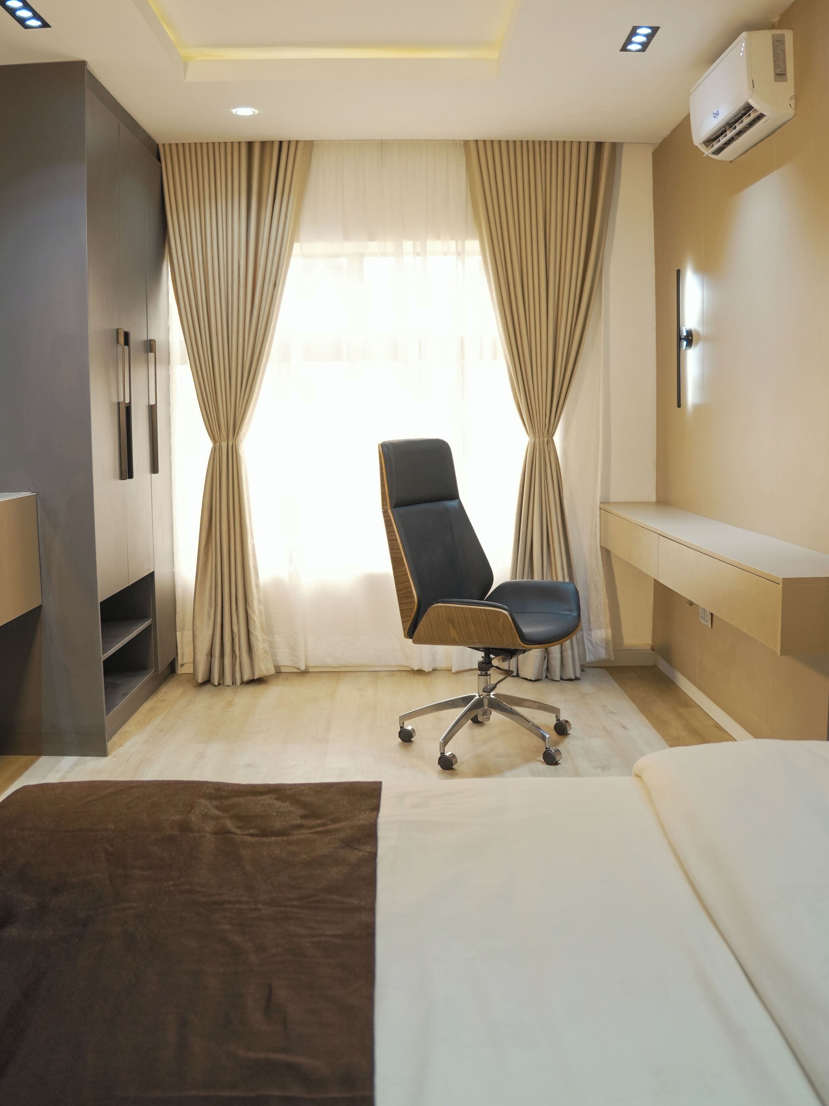 A hotel room with a bed, a desk, a chair, and an air conditioning unit.