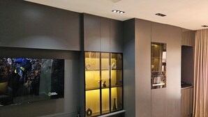A modern living room with a large flat-screen TV, built-in shelves, and recessed ceiling lighting. - Sapphire Suite (Abuja)