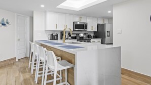 A modern kitchen with white cabinets, a central island with bar stools, a microwave, stove, and refrigerator.