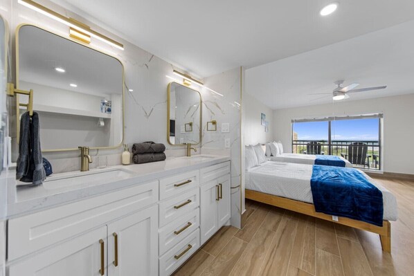 A modern bedroom with a large bed, a vanity with mirrors, and a balcony with a view.