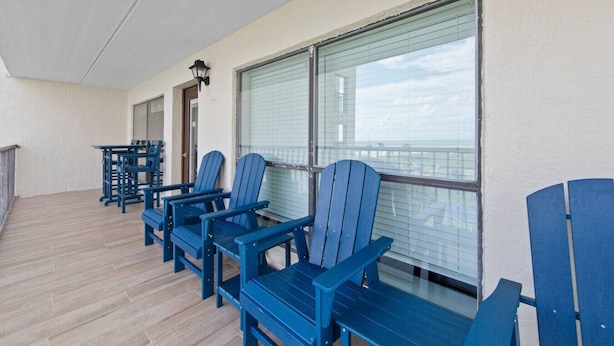 A balcony with blue Adirondack chairs, a table, and a lamp.