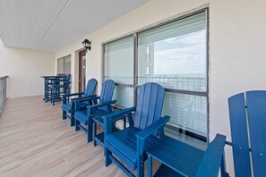 A balcony with blue Adirondack chairs, a table, and a lamp.