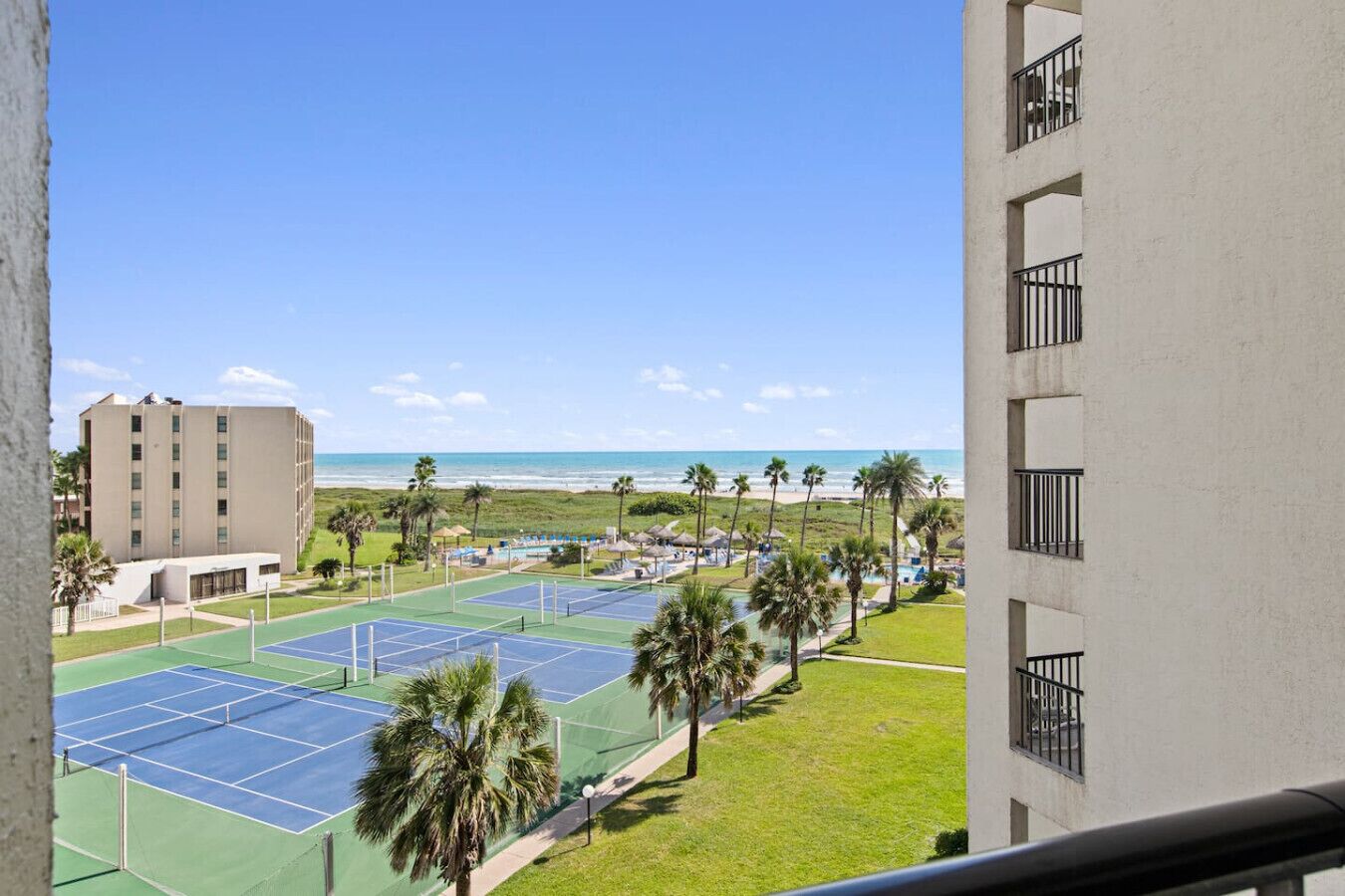 A view of a tennis court complex with a beach in the background.